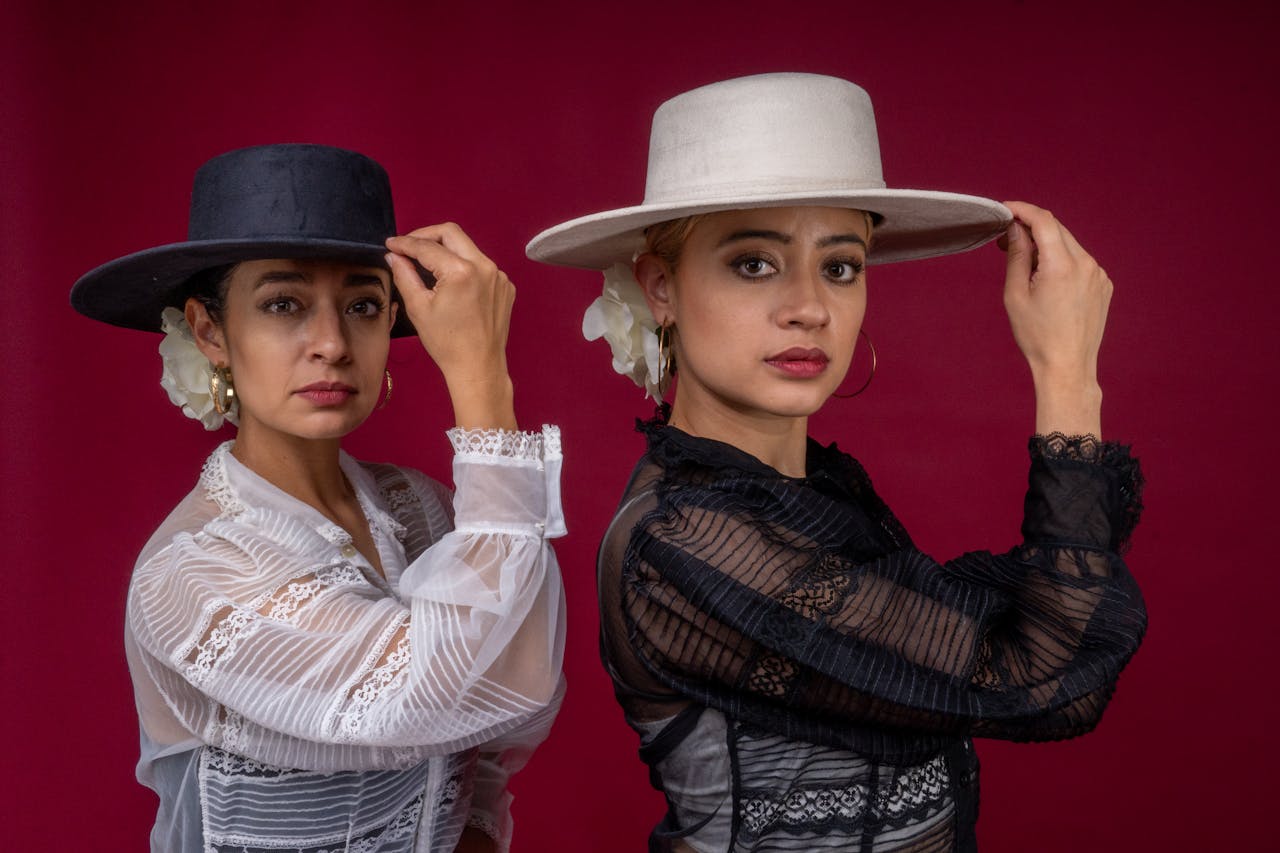 Home Two female flamenco dancers pose gracefully in traditional attire against a red backdrop.